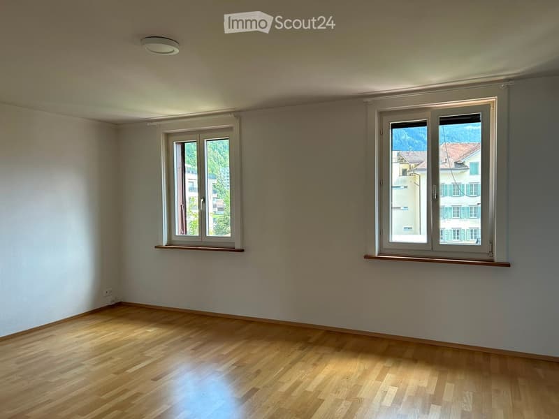 Empty room with wooden flooring, white walls, and two windows offering views of the outside. No furniture or equipment is present.