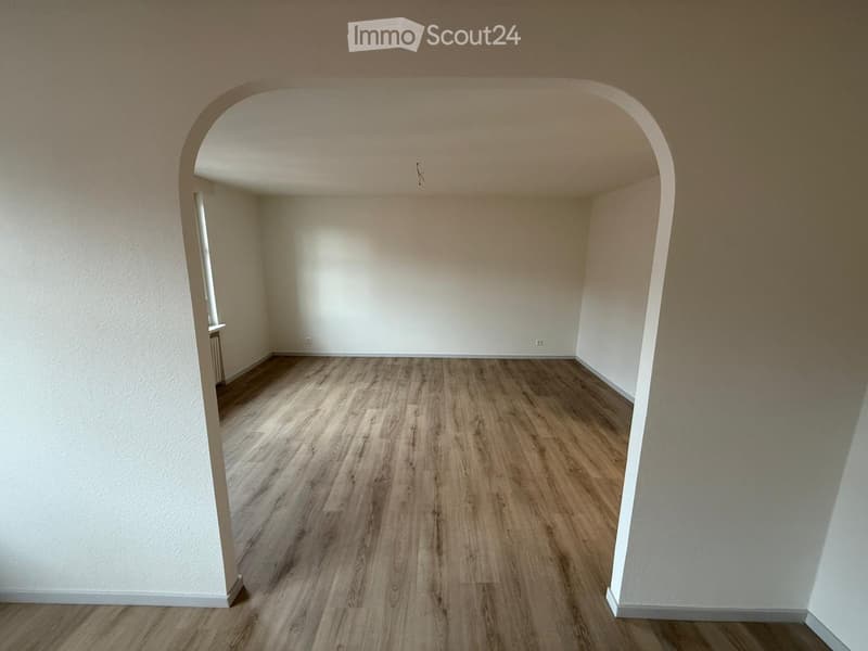 wooden floor, white walls, arched entrance, natural light from a window