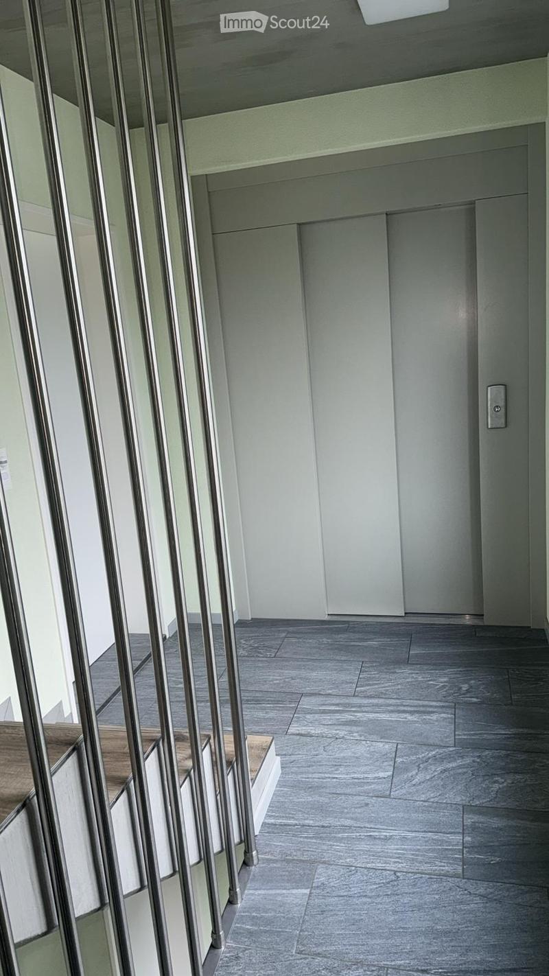 Modern hallway with grey tiled floor, white walls, and metal railings on the left side.