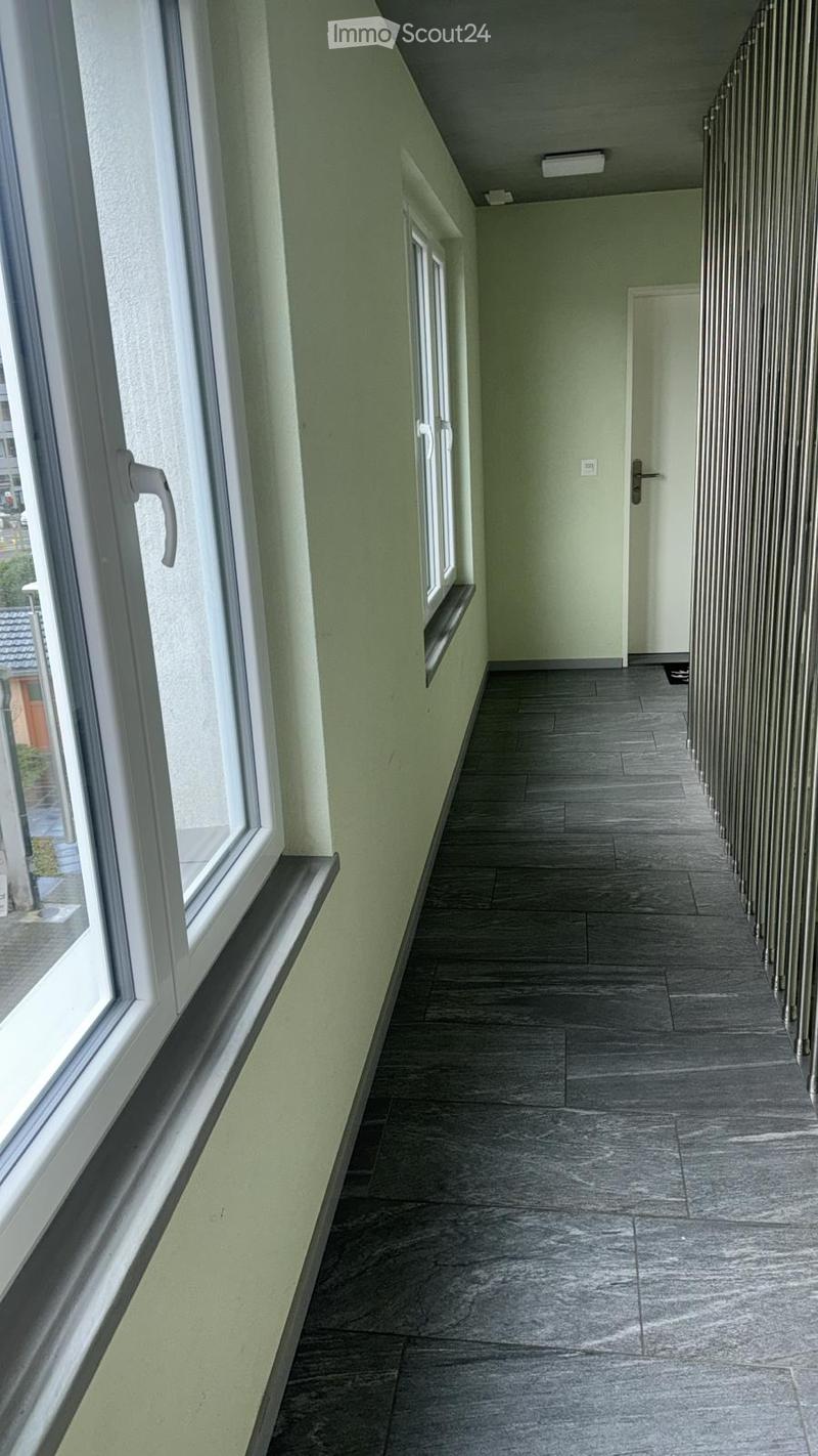 Empty hallway with grey tiled floor, light green walls, white window frames, and a closed door at the end.