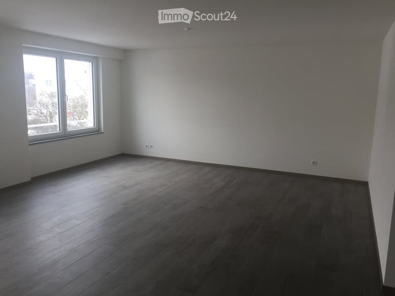 Empty room with wooden flooring, white walls, and large windows allowing natural light.