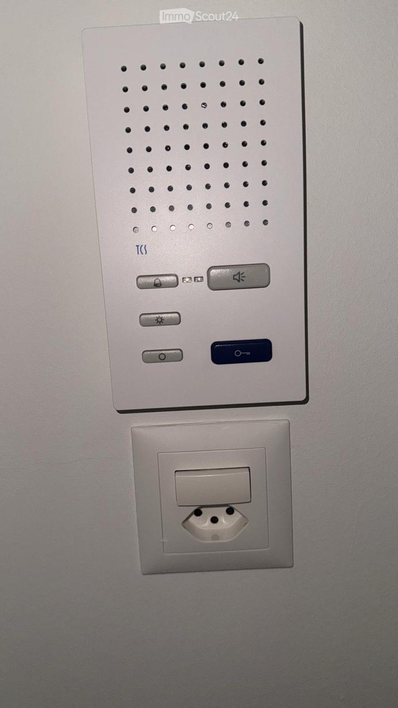 A modern wall-mounted light switch panel with multiple buttons and a standard electrical outlet below it.