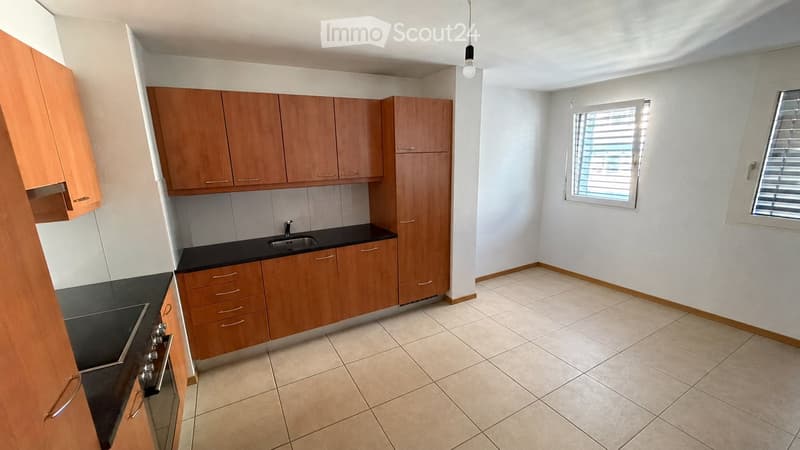 Modern kitchen with light wooden cabinets, black countertops, and tiled flooring. Features a sink, faucet, and stove.