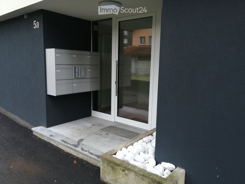 Modern building entrance with mailboxes, glass doors, and a small decorative rock garden.