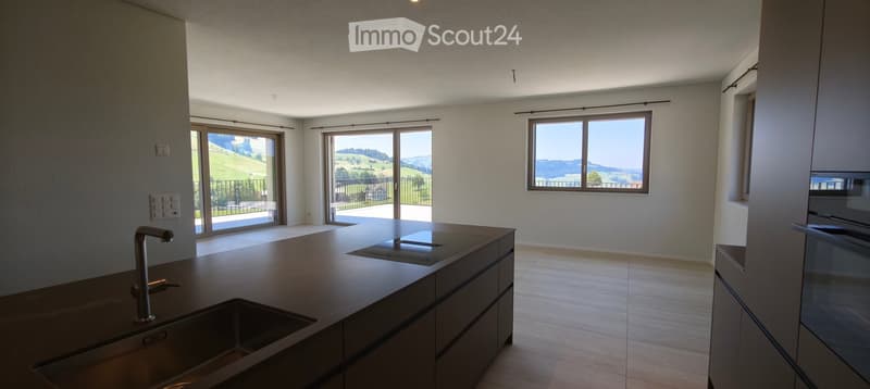 Modern kitchen with large windows offering scenic views, featuring a central island with a sink and faucet, and sleek cabinetry.