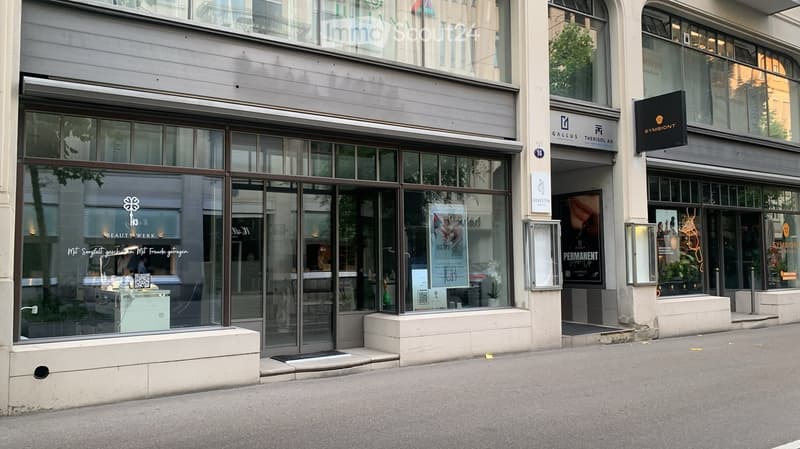 Modern urban building facade with large glass windows and storefronts, including a beauty salon and other commercial spaces.