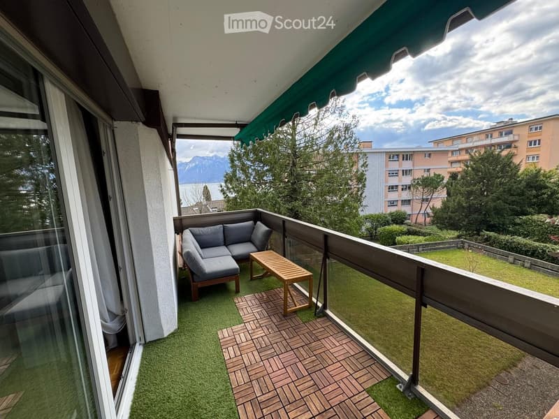 Balcony with green artificial turf, wooden decking, grey sofa, and small wooden table.