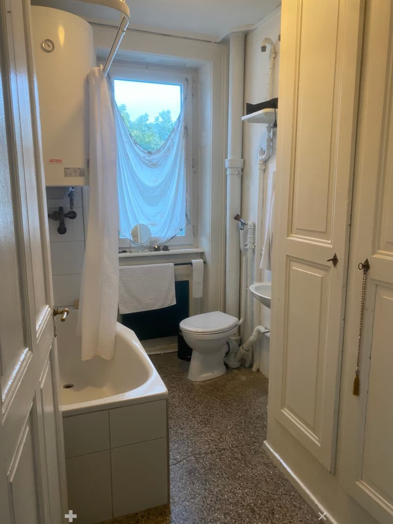 Bathroom with a bathtub, toilet, sink, and mirror. The room features a window with a curtain and a towel hanging on the side of the bathtub.
