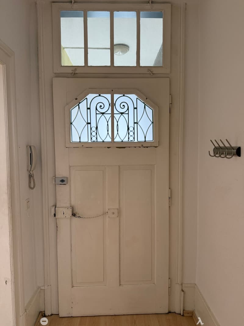 A narrow hallway with a closed door featuring a decorative glass panel above it, a small window above the door, and a coat rack on the right wall.