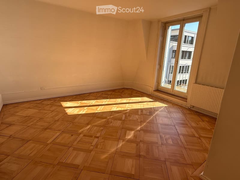 Empty room with wooden parquet flooring and large windows allowing natural light to enter.