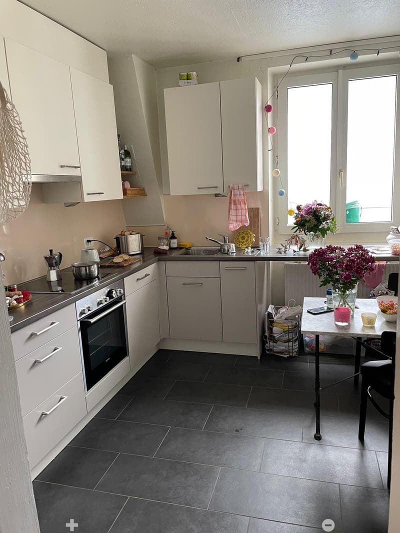 Modern kitchen with white cabinets, dark tiled floor, stainless steel appliances, and a small dining area with a table and chairs.