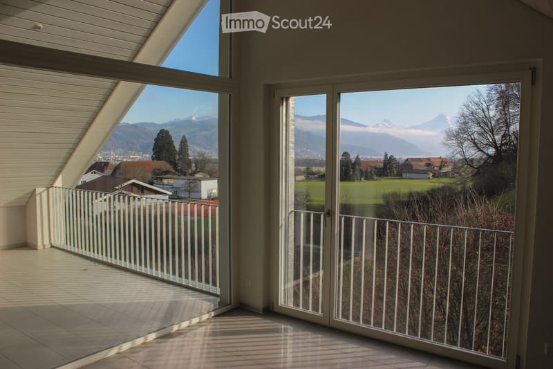 Bright balcony with large glass doors opening to a scenic view of mountains and countryside, featuring a white railing and tiled floor.