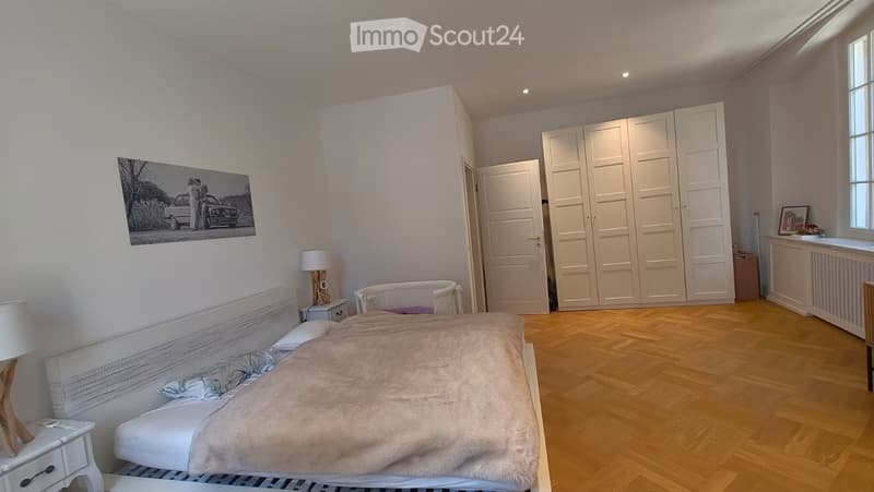 Well-lit bedroom with a large bed, nightstand, lamp, wardrobe, and a picture frame on the wall.