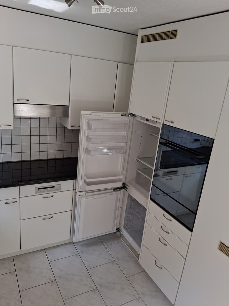 Modern kitchen with white cabinets, a stainless steel refrigerator, and an oven. The refrigerator doors are open, revealing empty shelves.