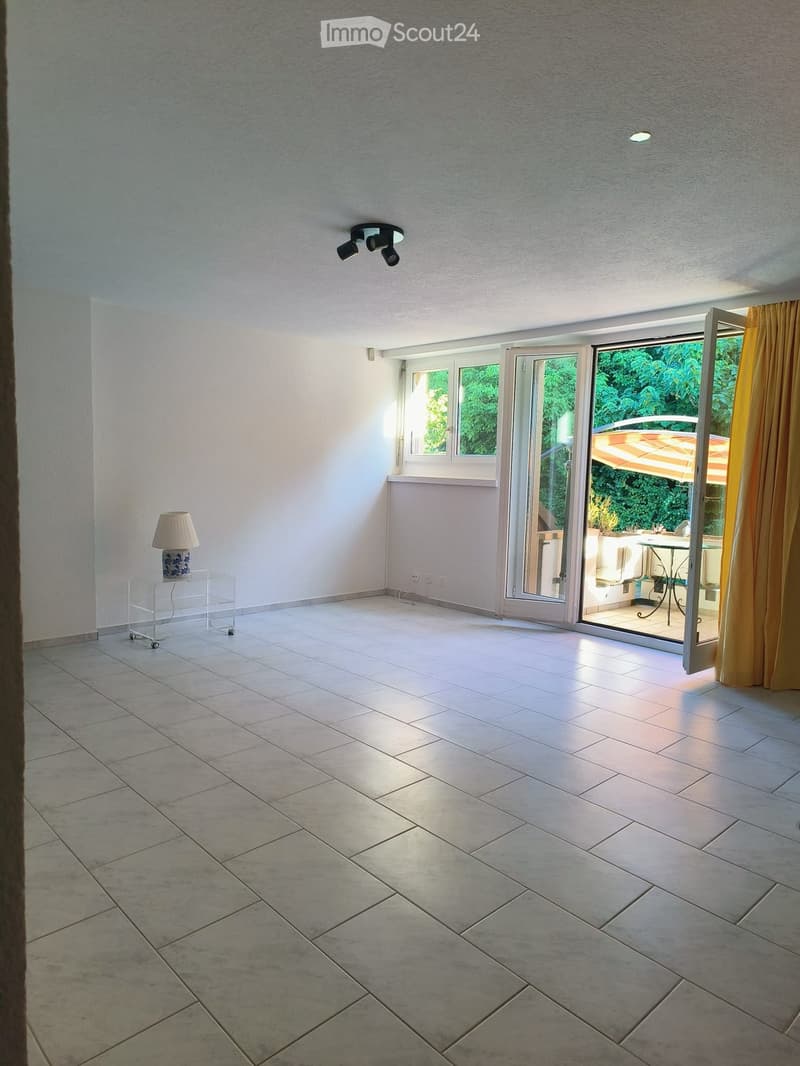 Empty room with tiled floor, white walls, large sliding glass doors leading to a patio, and a small table lamp on a glass stand.