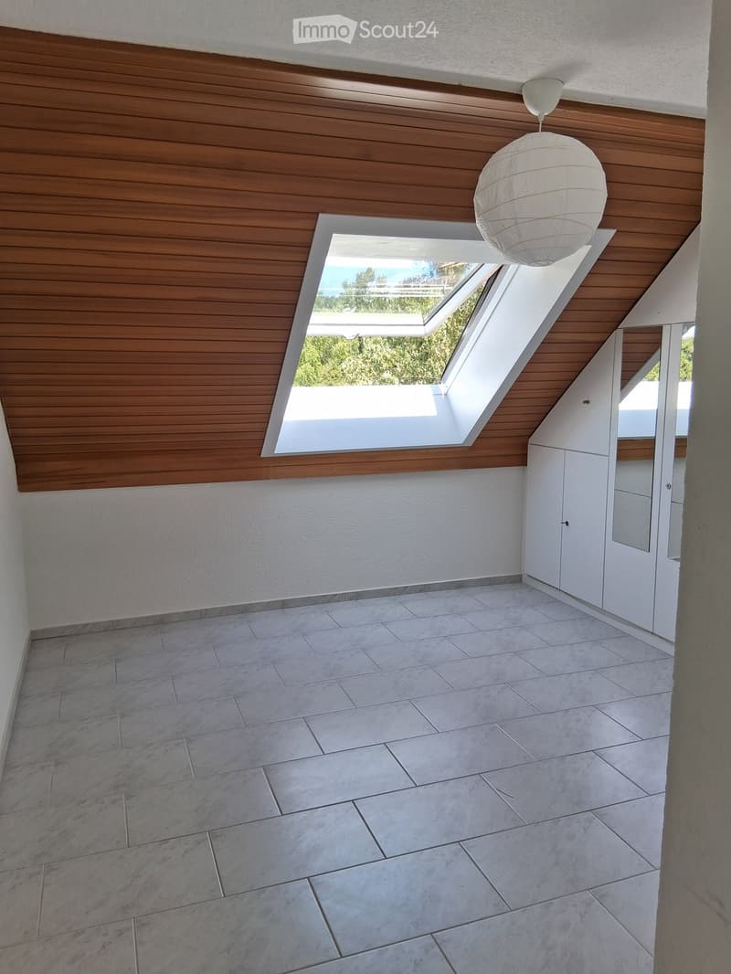 Empty room with wooden slat ceiling, skylight window, white walls, and tiled floor.