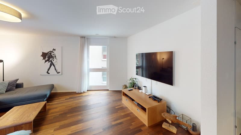 Modern living room with wooden flooring, a grey sofa, a wooden TV stand, a large flat-screen TV, and a decorative fish sculpture on the floor.