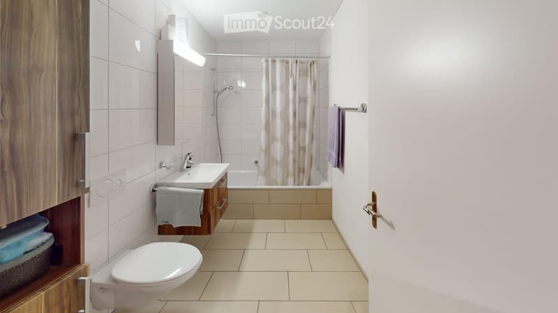 Modern bathroom with white tiles, a toilet, a sink with a wooden cabinet, a bathtub with a shower curtain, and a mirror above the sink.