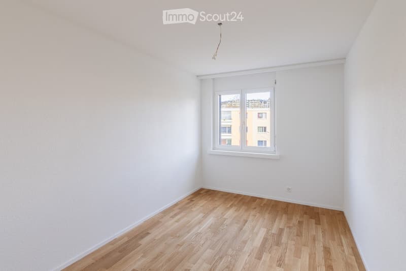 Empty room with white walls, wooden flooring, and a large window with white frame. No furniture or equipment present.