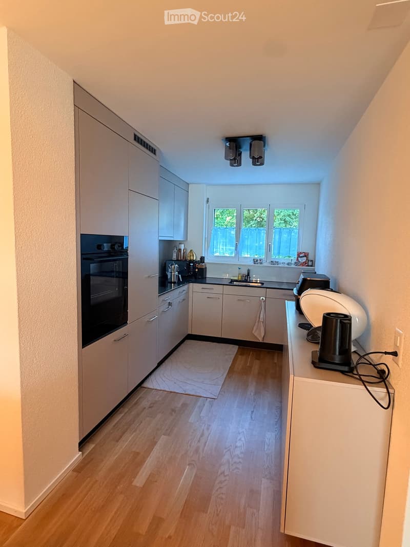 Modern kitchen with white cabinets, wooden flooring, and stainless steel appliances including an oven, sink, and coffee maker.