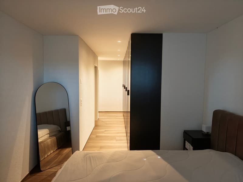 Modern bedroom with a large bed, nightstand, and a full-length mirror on the wall.
