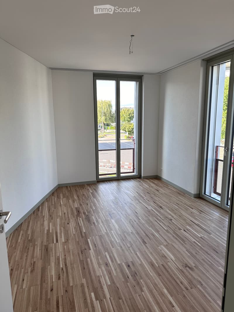 Empty room with wooden flooring, white walls, and large glass sliding doors leading to an outdoor area.