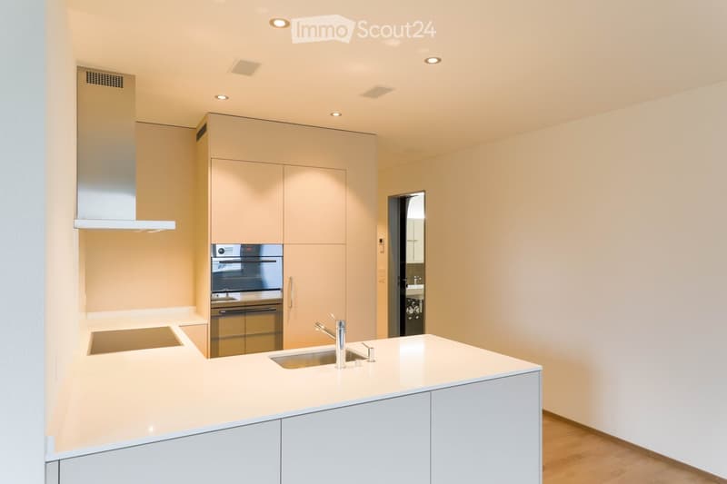 Modern kitchen with light-colored cabinets, a white countertop, a stainless steel sink, and an oven. The space features recessed lighting and a sleek design.