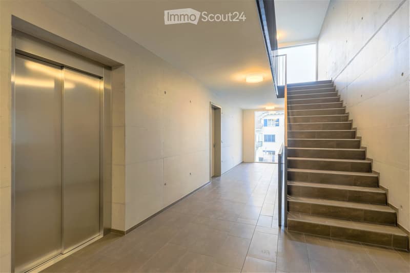 Modern hallway with tiled flooring, a staircase leading upwards, and an elevator on the left side.