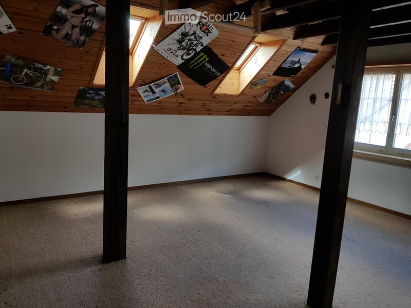 Empty attic room with wooden slanted ceilings, skylights, and white walls. No furniture or equipment present.