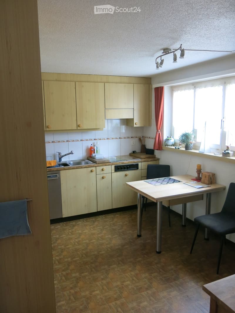 Bright kitchen with light wooden cabinets, tiled backsplash, and a window with a plant on the sill. Includes a sink, dishwasher, table, and chairs.