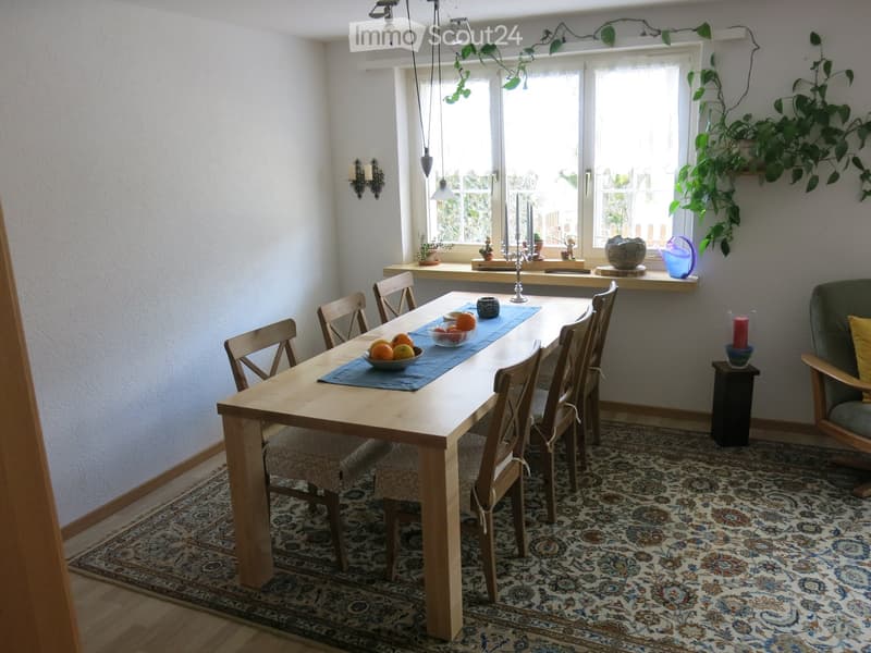 Dining room with a wooden dining table, six chairs, a patterned rug, a sofa, and decorative items on the windowsill.