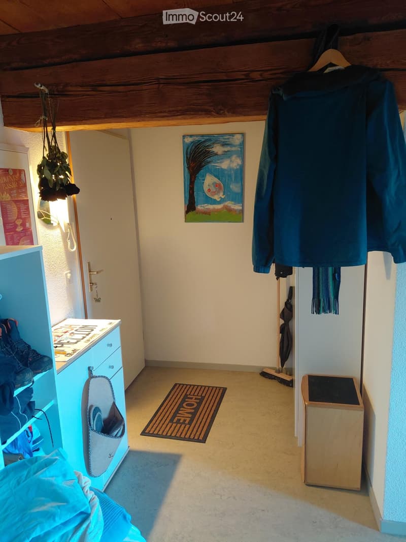Hallway with wooden ceiling beams, a doormat reading "HOME", a coat rack with jackets, a shoe cabinet, and a small painting on the wall.