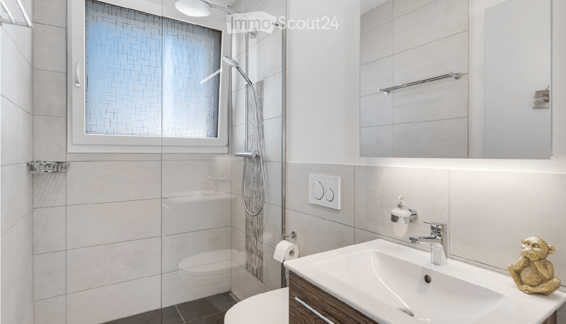 Modern bathroom with a glass-enclosed shower, a sink with a modern faucet, a toilet, a large mirror, and a decorative golden statue on the sink counter.