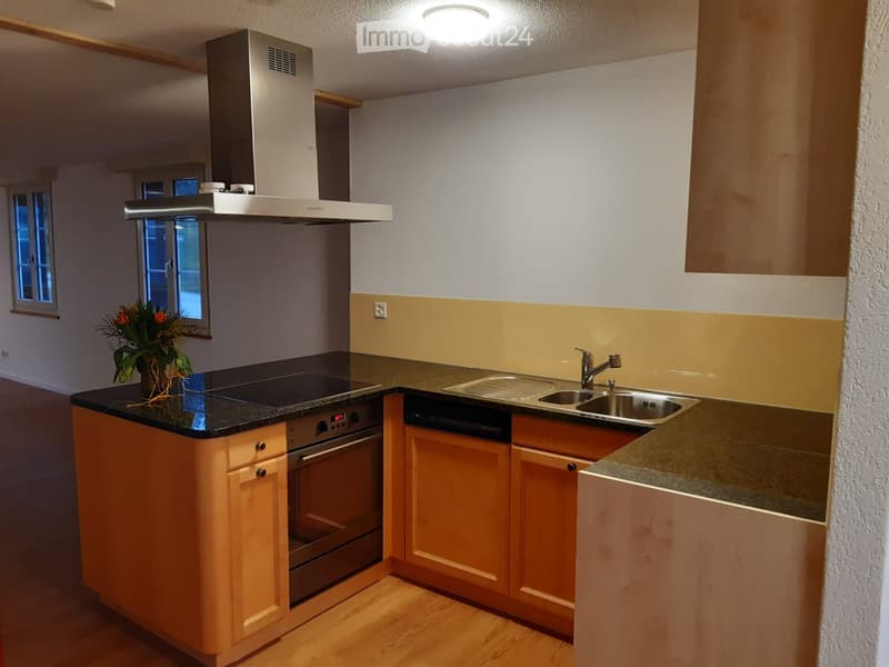 Modern kitchen with wooden cabinets, black countertop, stainless steel appliances, and a window with a flower vase on the counter.