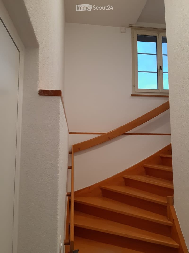Wooden staircase with a handrail, white walls, and a window at the top of the stairs.