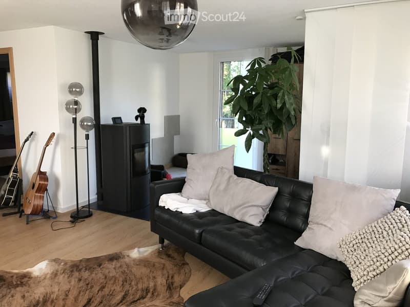 Modern living room with a black leather sofa, pillows, a blanket, a floor lamp, guitars, a large mirror, and a balloon light fixture.