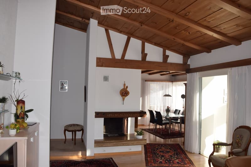 Bright living and dining area with exposed wooden beams, fireplace, dining table with chairs, sofa, and decorative items.