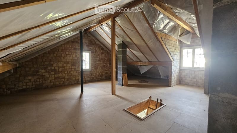 Empty attic space with exposed wooden beams, brick walls, and skylights. Features a wooden floor and a small opening in the floor.
