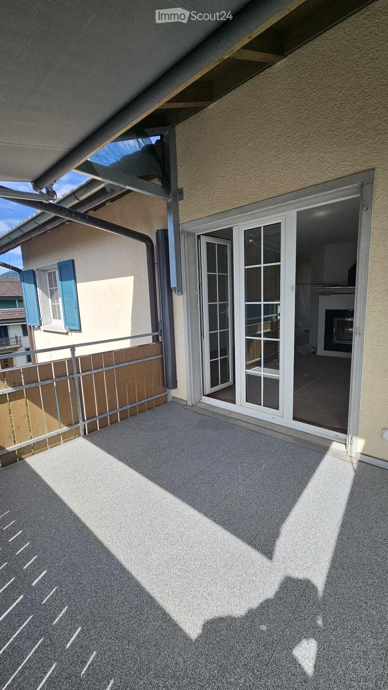Balcony with grey carpeted floor, metal railing, and sliding glass doors leading to an interior space.