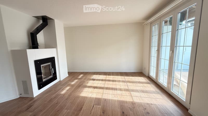 Empty room with wooden flooring, white walls, and a fireplace with a black insert. Large glass doors lead to an outdoor area.