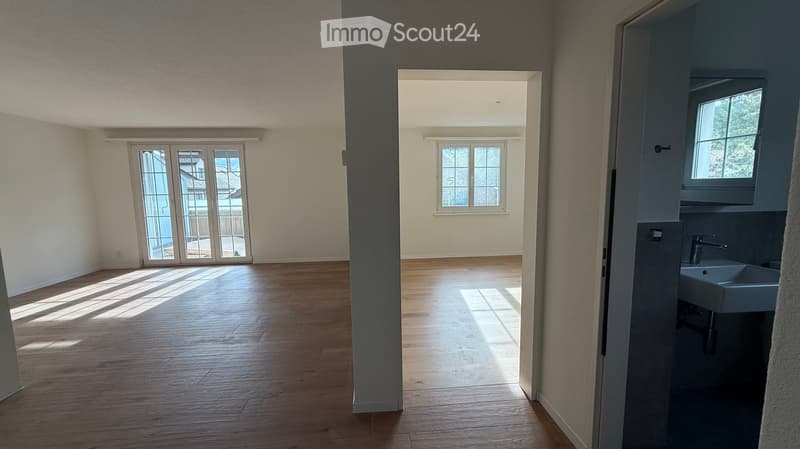 Empty room with wooden flooring, large windows, and a sink in the corner.