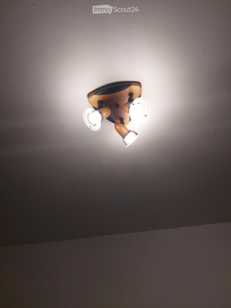 Empty room with a ceiling-mounted light fixture featuring two adjustable spotlights. The walls and ceiling are plain and unpainted.