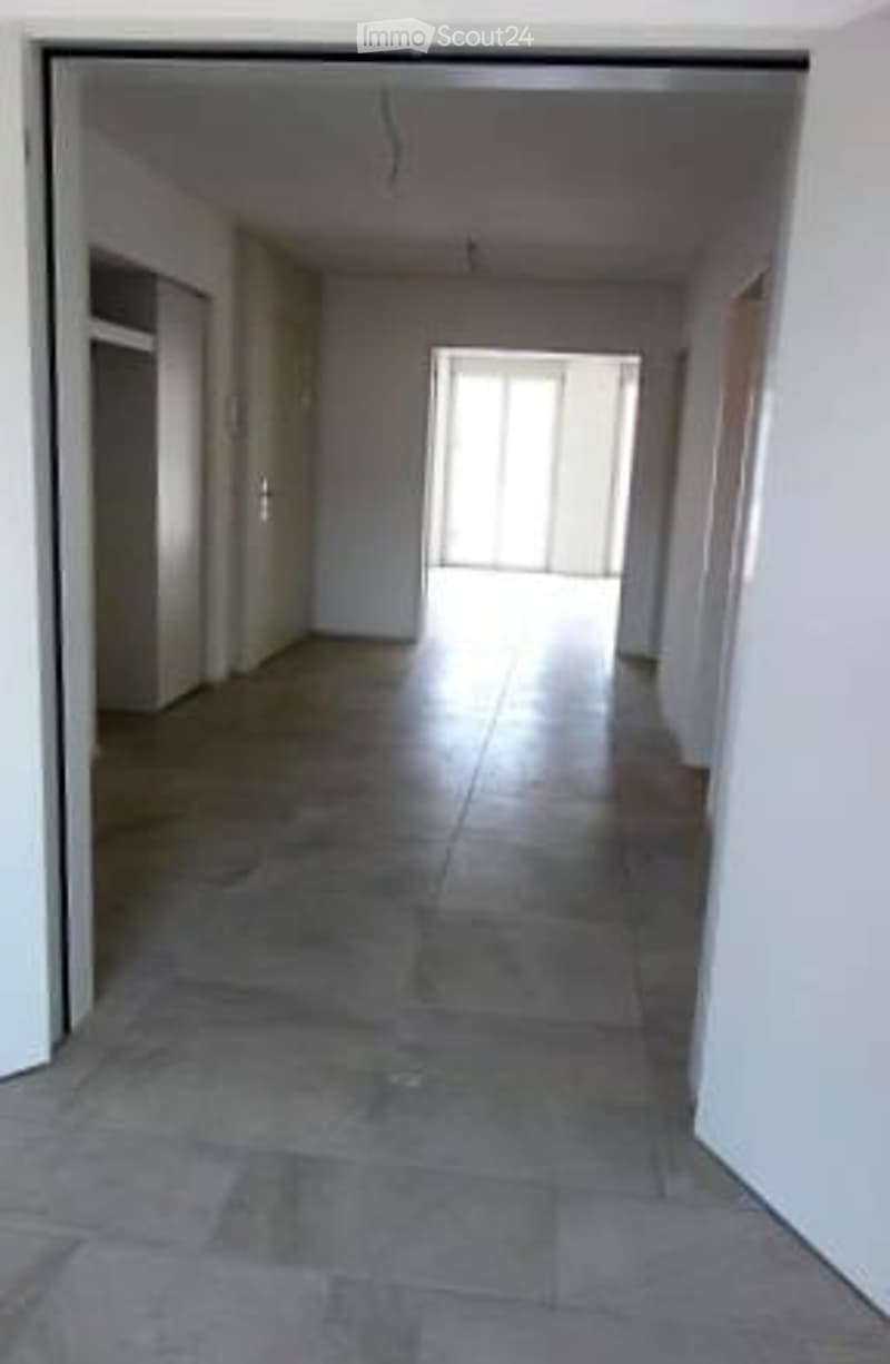 Empty hallway with tiled floor and white walls, leading to a bright doorway at the end.