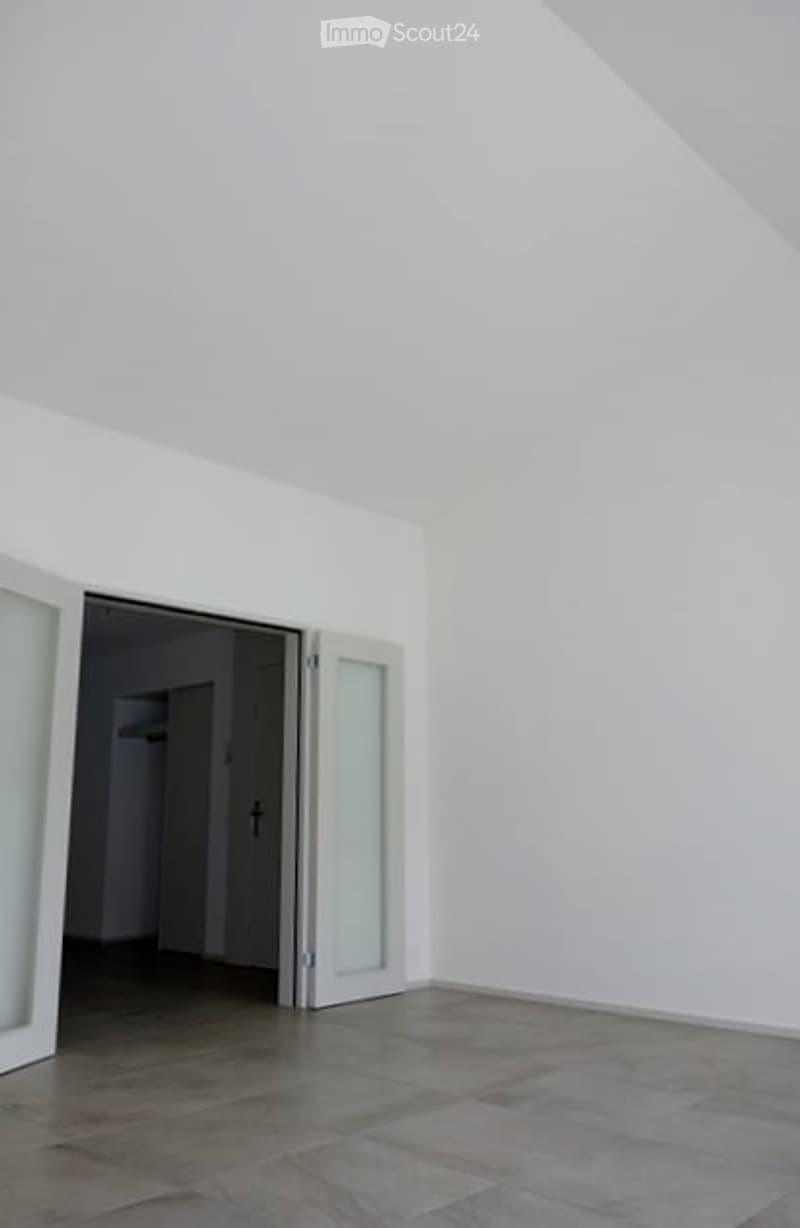 Empty room with white walls, grey tiled floor, and large glass sliding doors leading to another space.
