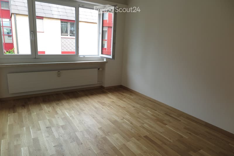 Empty room with light wooden flooring, white walls, and large windows with open shutters, allowing natural light to fill the space.