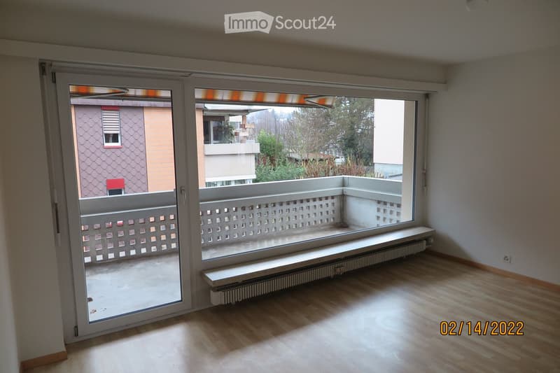 Empty room with wooden flooring, large windows, radiator, and sliding glass doors leading to a balcony.
