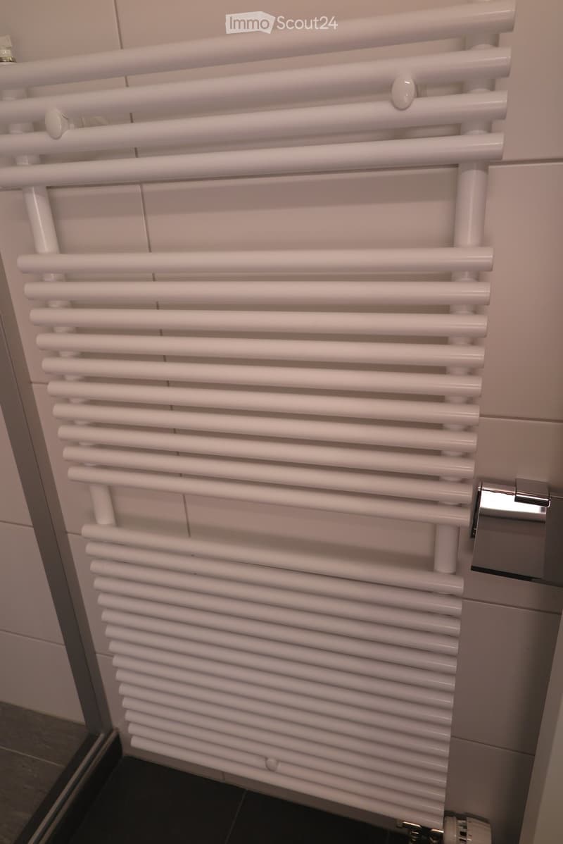 White radiator with multiple horizontal bars mounted on a tiled wall in a bathroom.