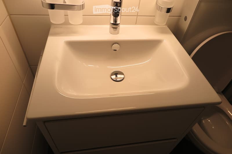 Modern bathroom sink with a sleek, white countertop and chrome faucet, integrated into a dark-toned cabinetry.