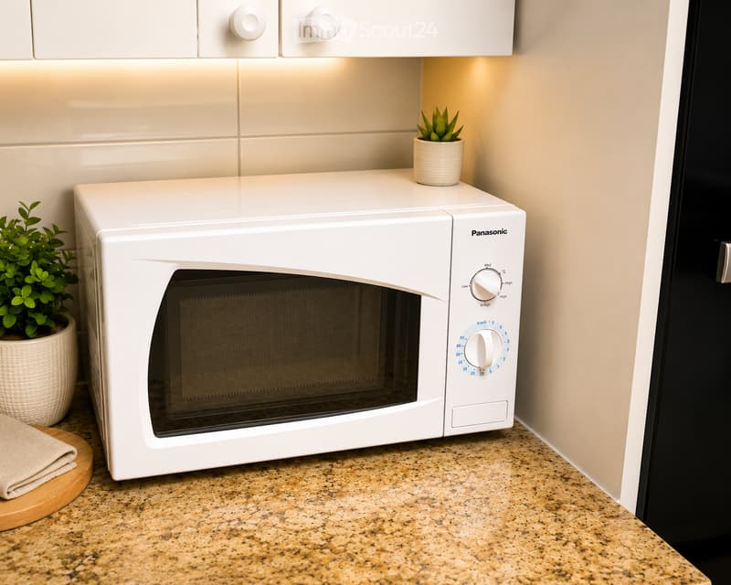A modern kitchen with a white microwave, granite countertop, and small potted plants on the counter.