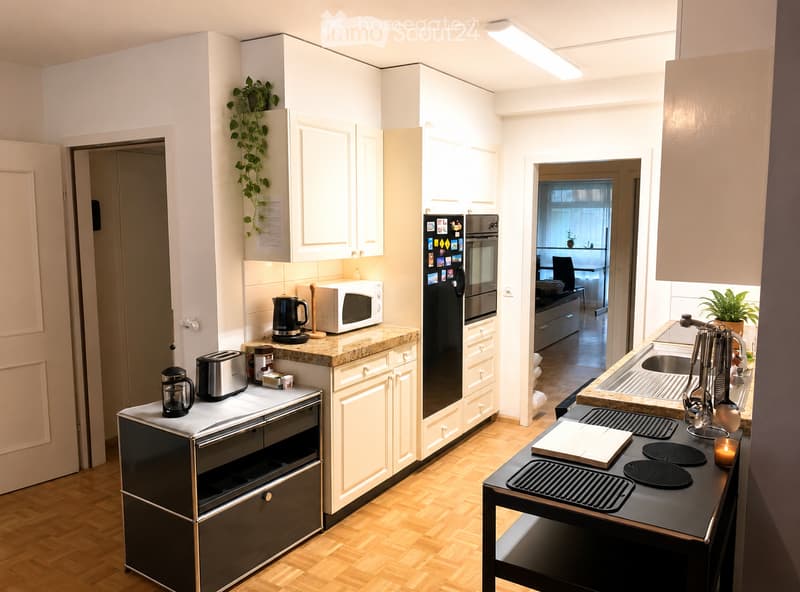 Modern kitchen with white cabinets, granite countertops, stainless steel appliances, and a small dining area visible through an open doorway.